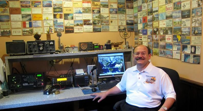 Don Greenbaum with his radios, in front of postcards from all the places he's called.