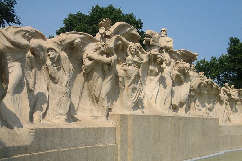 A long concrete sculpture featuring a procession of human figures in flowing robes under a clear blue sky.