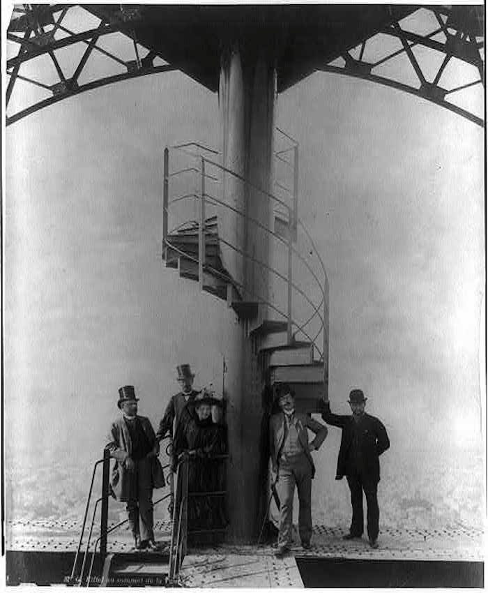 Gustave Eiffel and others standing astride one of the tower's spiral staircases in 1889.