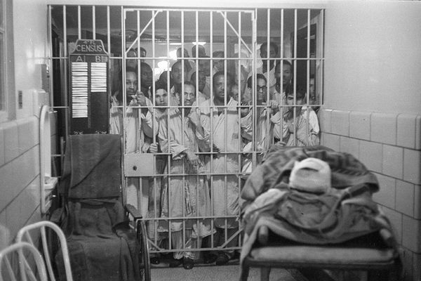 Prisoners at Rikers Island watch through bars as an injured airline passenger waits for transport to a New York hospital.
