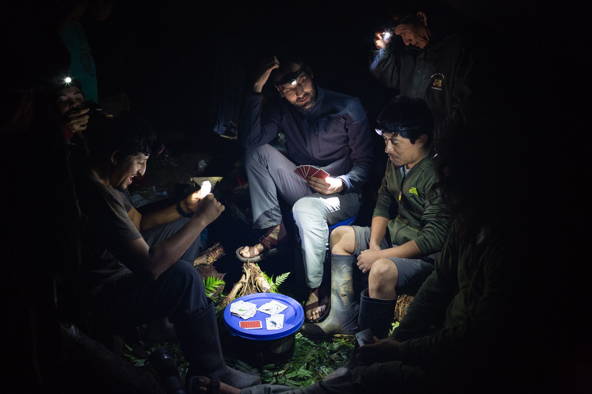 The team members play cards by the light of their headlamps.