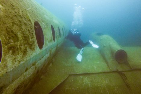 A diver swims along the side of the plane wreck