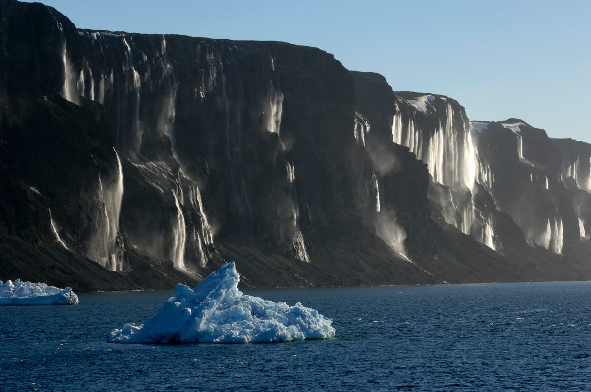 Backlit waterfalls shimmer down the side of Vega Island's dark cliffs.