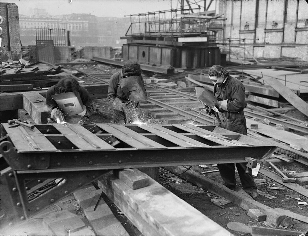 A photo from The Daily Herald, with the original caption "Girl acetylene welders were at their job as usual today, cutting the girders of the temporary Waterloo Bridge, which is being dismantled." 