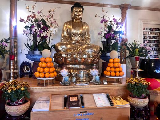 A buddhist altar with a golden seated buddha flanked by flowers and oranges.