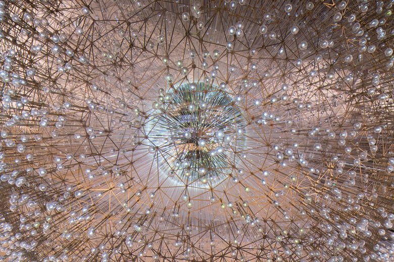 A large spherical light sculpture made of a dense web of gold wires and hundreds of glowing glass orbs.