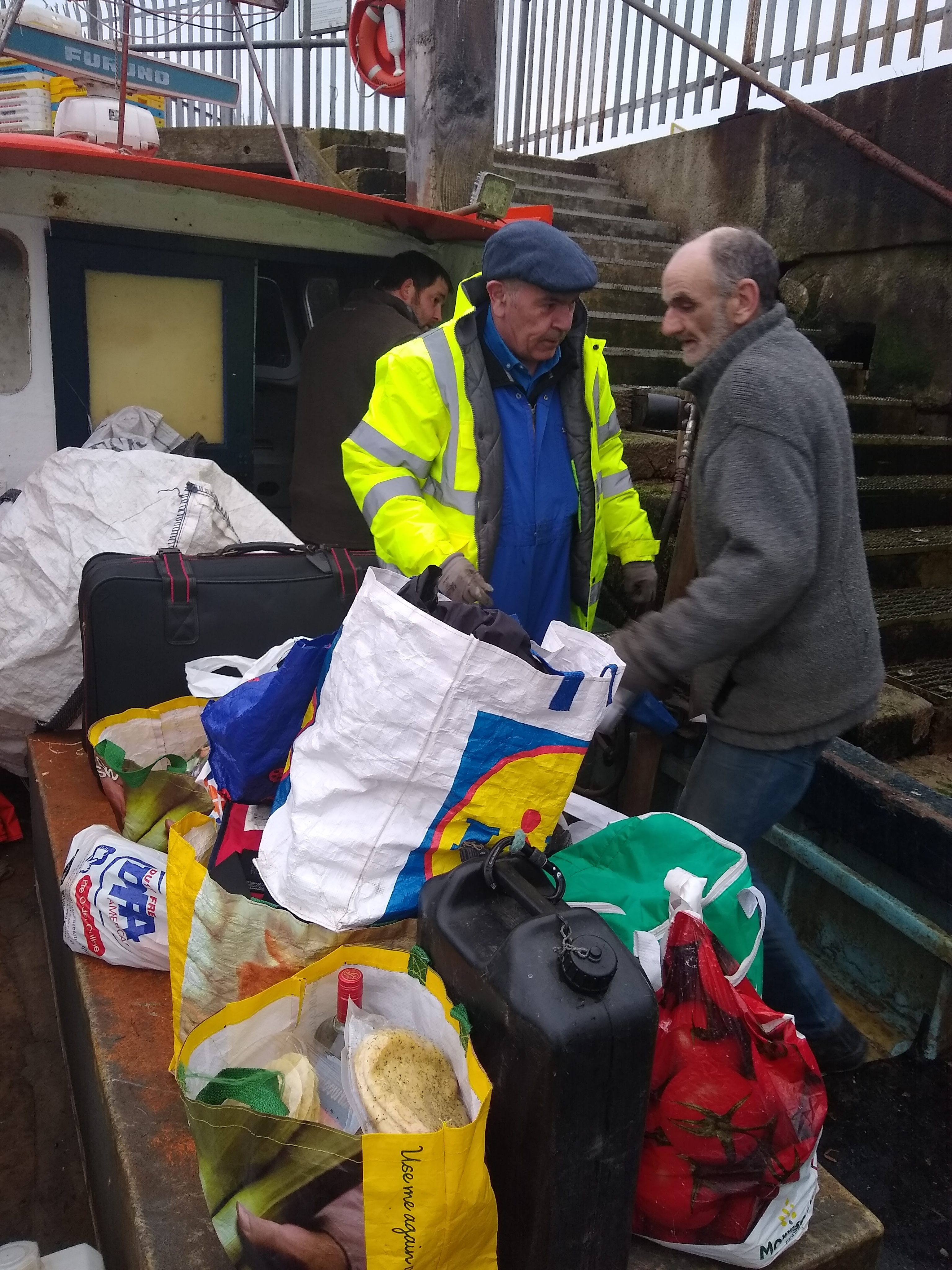 Joe Hamill (in neon jacket) and local fisherman Pecker load Hamill's supplies onto a boat for a two-week stretch in Sealand.