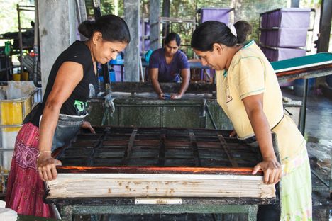Two women create a fabric-pulp sheet.
