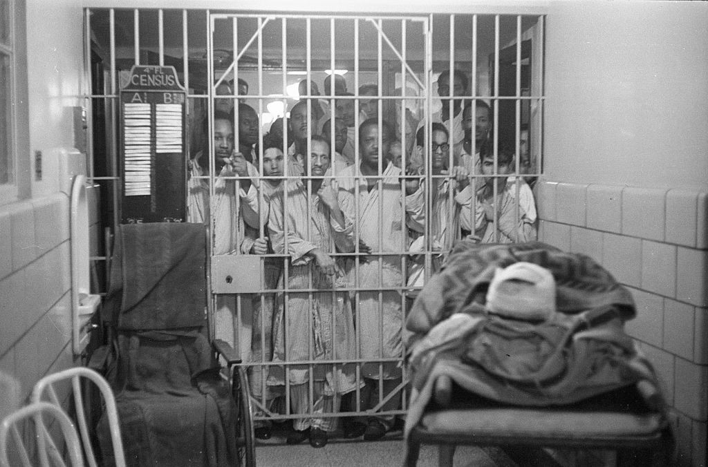 Prisoners at Rikers Island watch through bars as an injured airline passenger waits for transport to a New York hospital.
