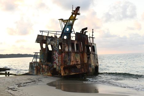 A rusty shipdeck sits submerged in the sand along a beach