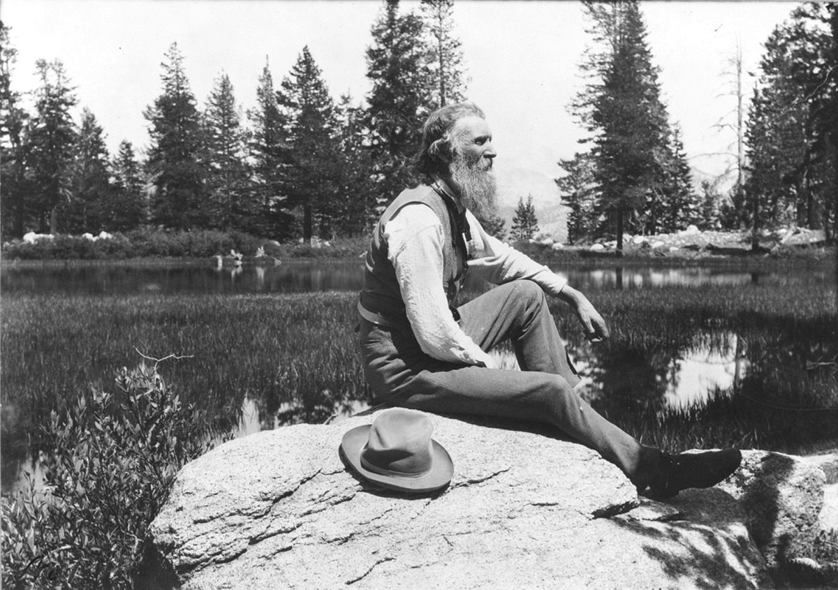 Muir, pictured later in life, seated on a rock.
