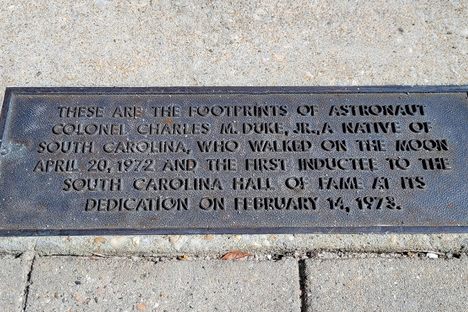 A plaque detailing information about astronaut Charles Duke, his moon walk, and his induction into the South Carolina Hall of Fame, sits just beneath the imprints of his moon boots outside the Myrtle Beach Convention Center.