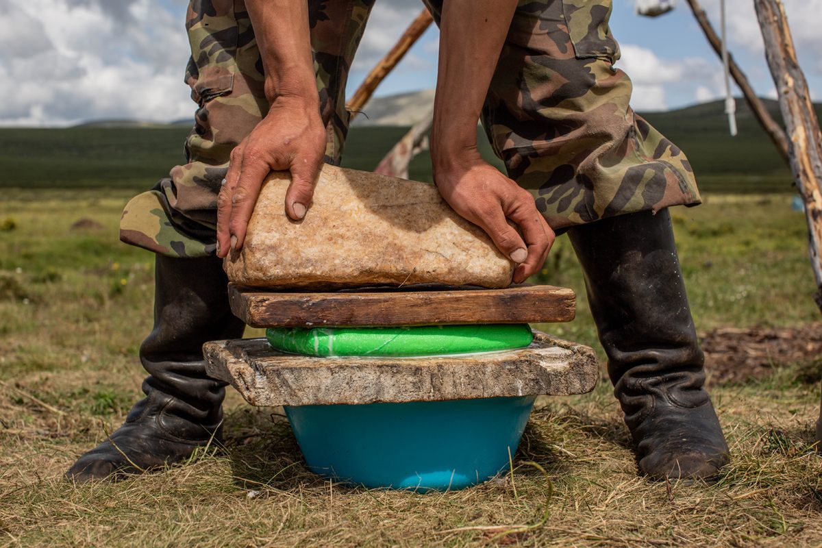 Ganbat uses a rock that holds down a side of their ger to help mold the cheese.
