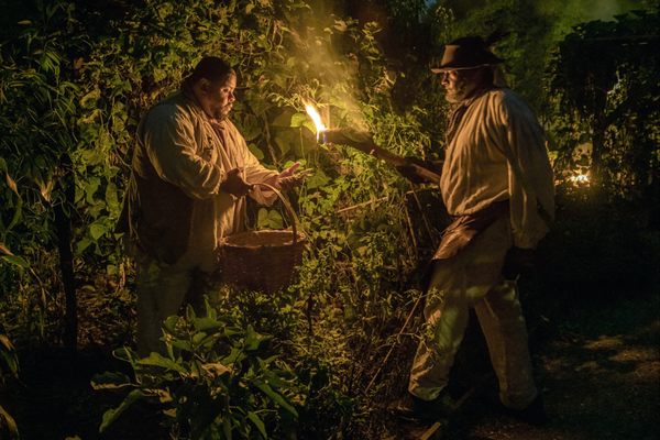Culinary historian Michael Twitty (left) and interpreter Robert Watson pick case-knife beans by torch light at the Sankofa Heritage Garden.