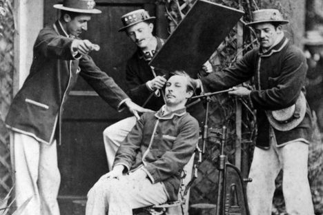 A sitter is clamped into position using a metal frame before having his portrait taken. 