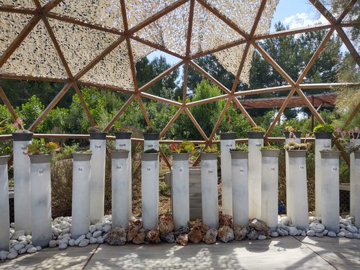 Some two dozen white tubes sit in front of a triangle lattice wall