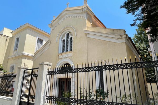 A cream-colored Greek church behind a black iron fence and gate