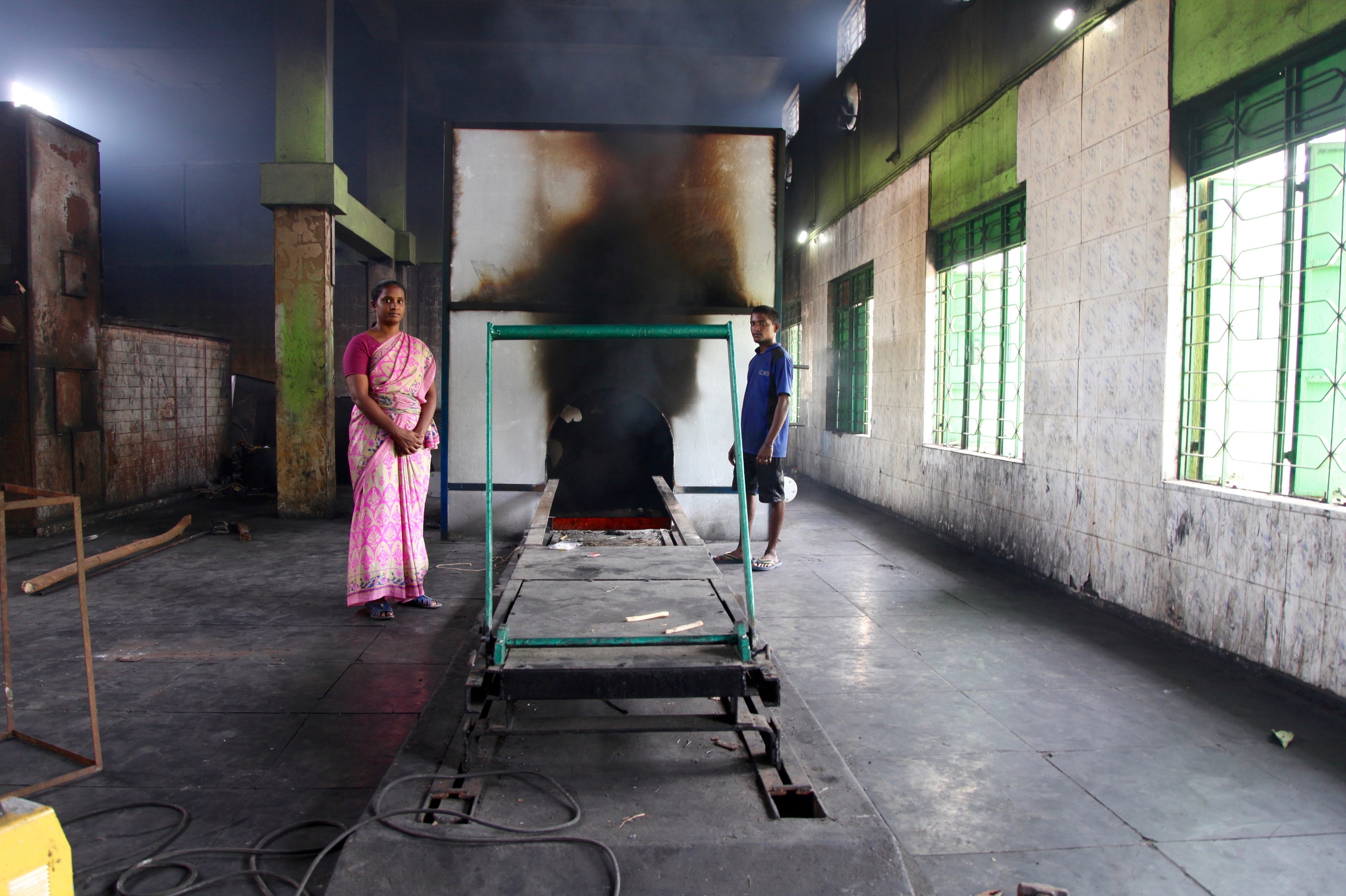 Crematorium assistant Divya Raju and a furnace operator pose in front of an active furnace.