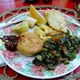 A breakfast of ackee and saltfish served with callaloo greens, a biscuit, and fruit.