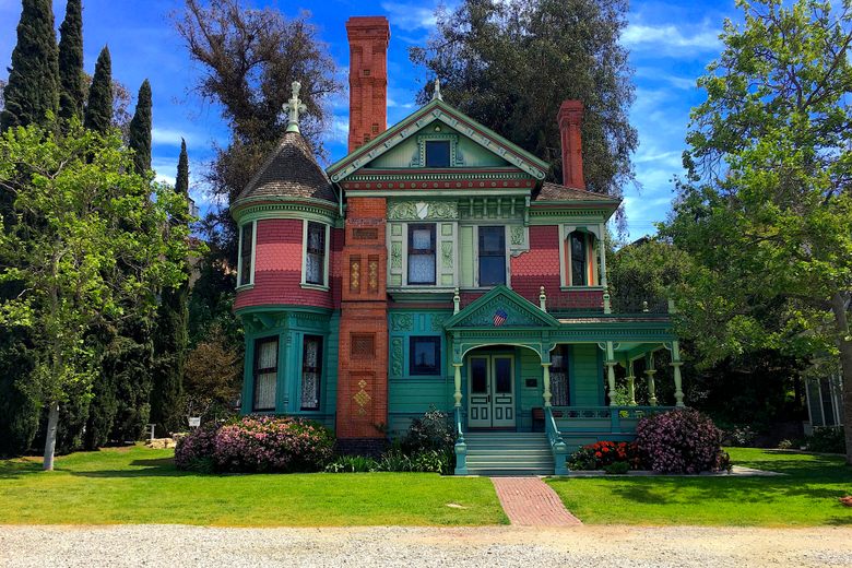 A colorful Victorian house with green, red, and teal siding features a turret and a tall brick chimney.