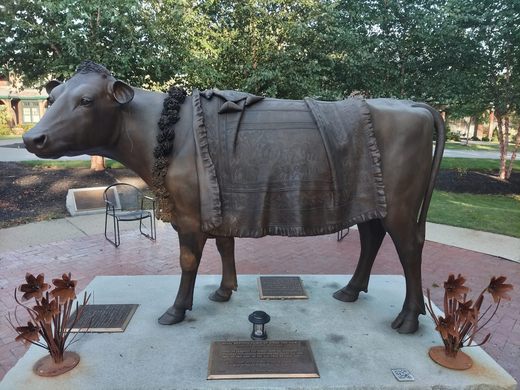A bronze statue of a cow with blanket and flower garland around her neck