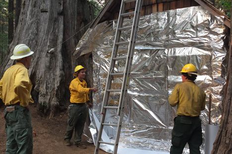 Forest Service workers wrap a historic cabin in foil.