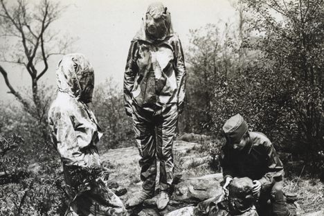 Three camoufleurs in the Women’s Reserve Camouflage Corps  make one woman disappear into the forest floor. 