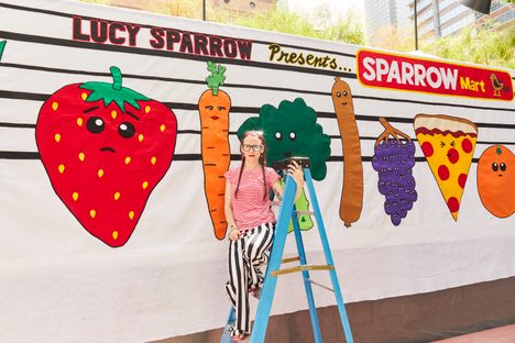 Lucy Sparrow stands in front of the fully felted sign for Sparrow Mart. 