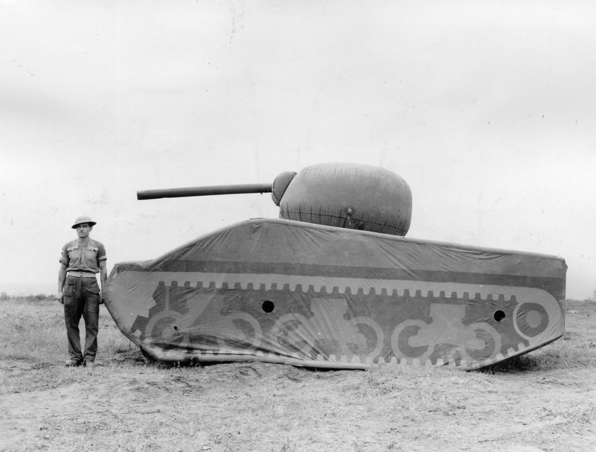 A soldier stands next to an inflated dummy tank made of rubber.