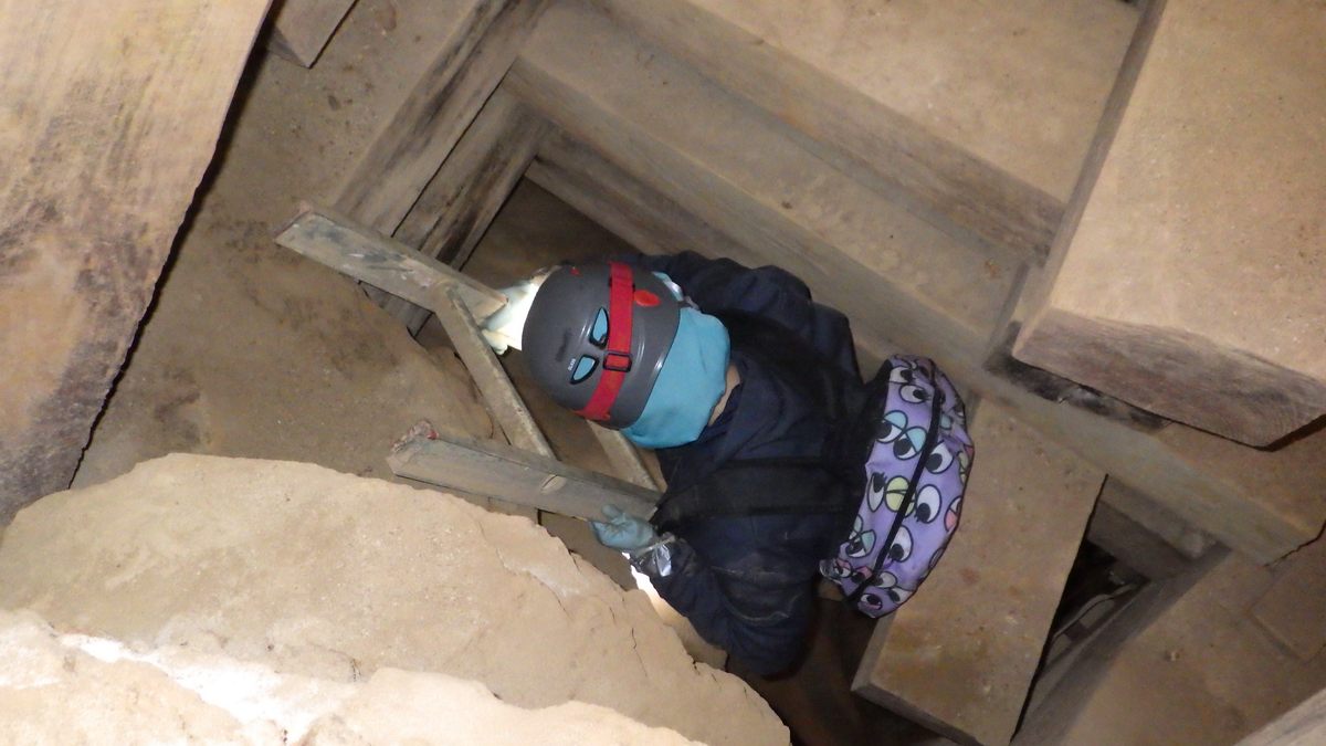 Confortin lowers herself carefully into a narrow mineshaft.