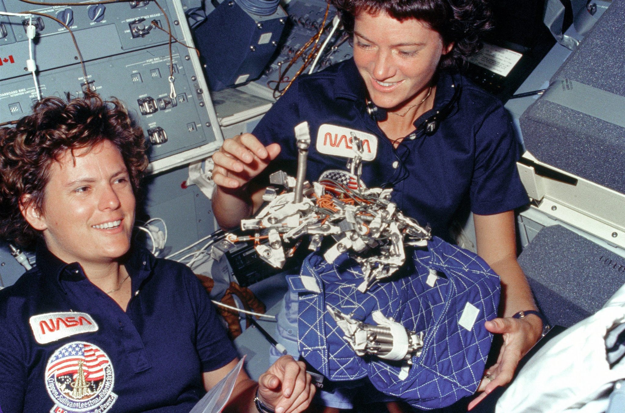  (October 6, 1984) Astronauts Kathryn D. Sullivan, left, and Sally K. Ride display a "bag of worms." The "bag" is a sleep restraint and the majority of the "worms" are springs and clips used with the sleep restraint in its normal application. Clamps, a bungee cord and velcro strips are other recognizable items in the "bag.