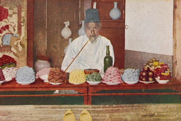 A shopkeeper in Seoul selling piles of festival treats, in the early 20th. 