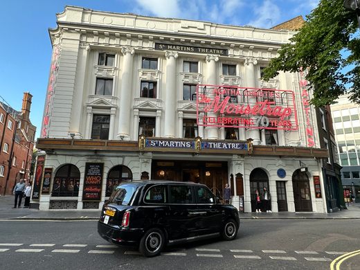 The white exterior of a Victorian theater with red neon lettering 