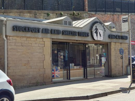 A museum entrance with sliding glass doors below a sign in blue letters that says "Stockport Air Raid Shelters"