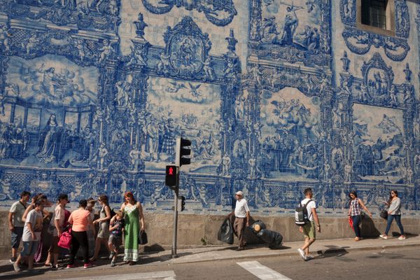 People walk in front of the azulejo tiles on the exterior of Capela Das Almas in Porto.