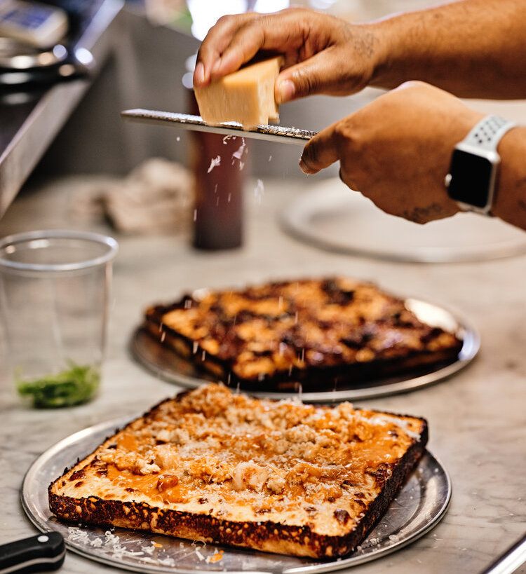 A Detroit-style pizza gets topped with a liberal helping of Parmesan cheese.