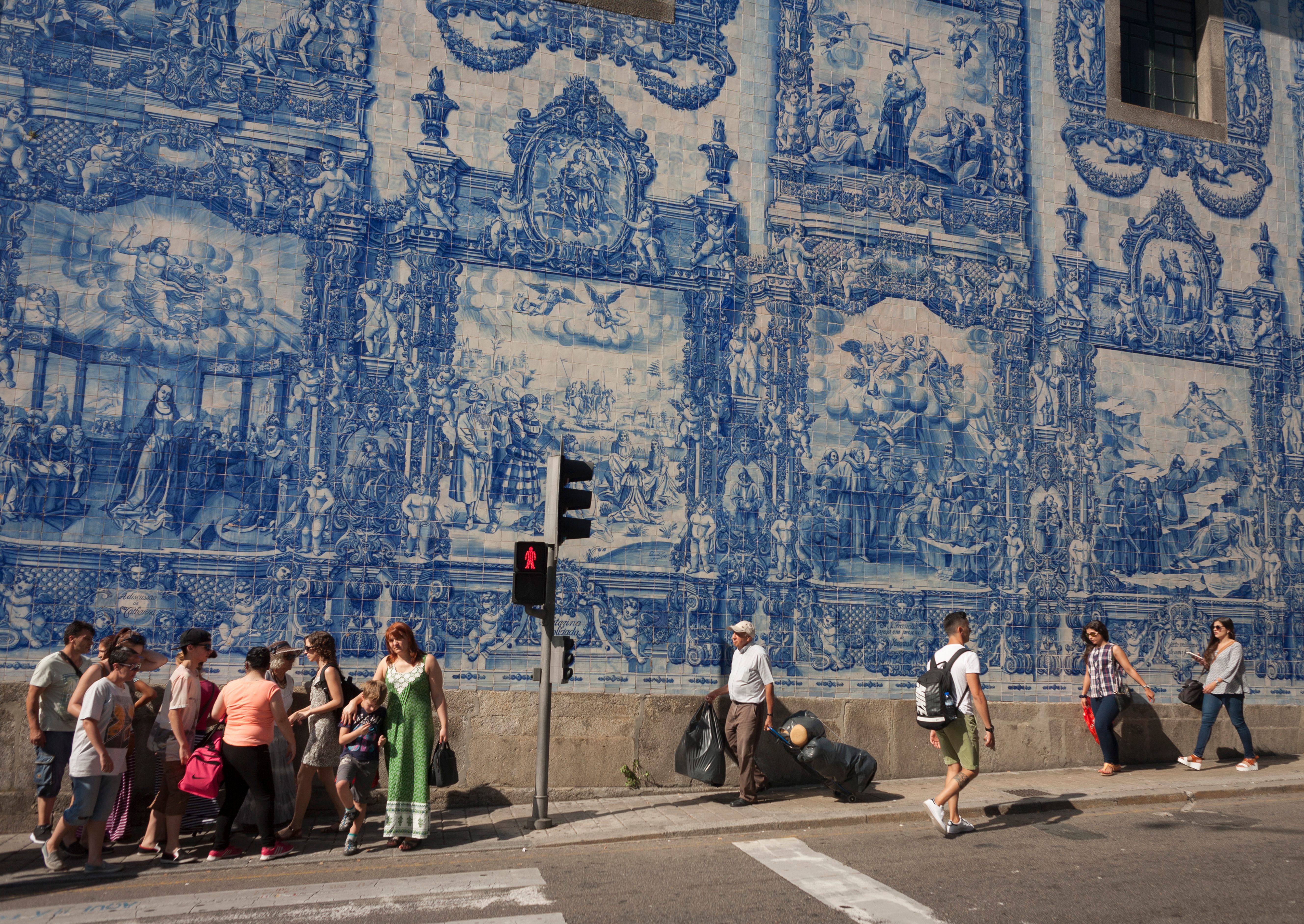 People walk in front of the azulejo tiles on the exterior of Capela Das Almas in Porto.