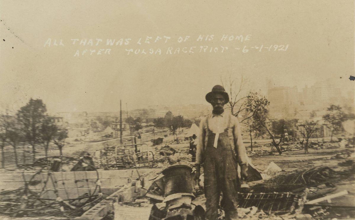 A historical postcard shows a man standing in front of the ruins of his home.