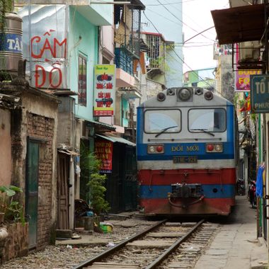 Diesel train coming down the train tracks through a narrow street in Hanoi.