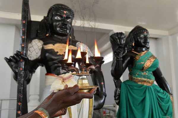 A Hindu priest holds a lit coconut oil lamp in front of statues of Prince Vijaya (left) and Kuweni (right) at the Sri Subramaniam temple in the southern Sri Lankan town of Matara.