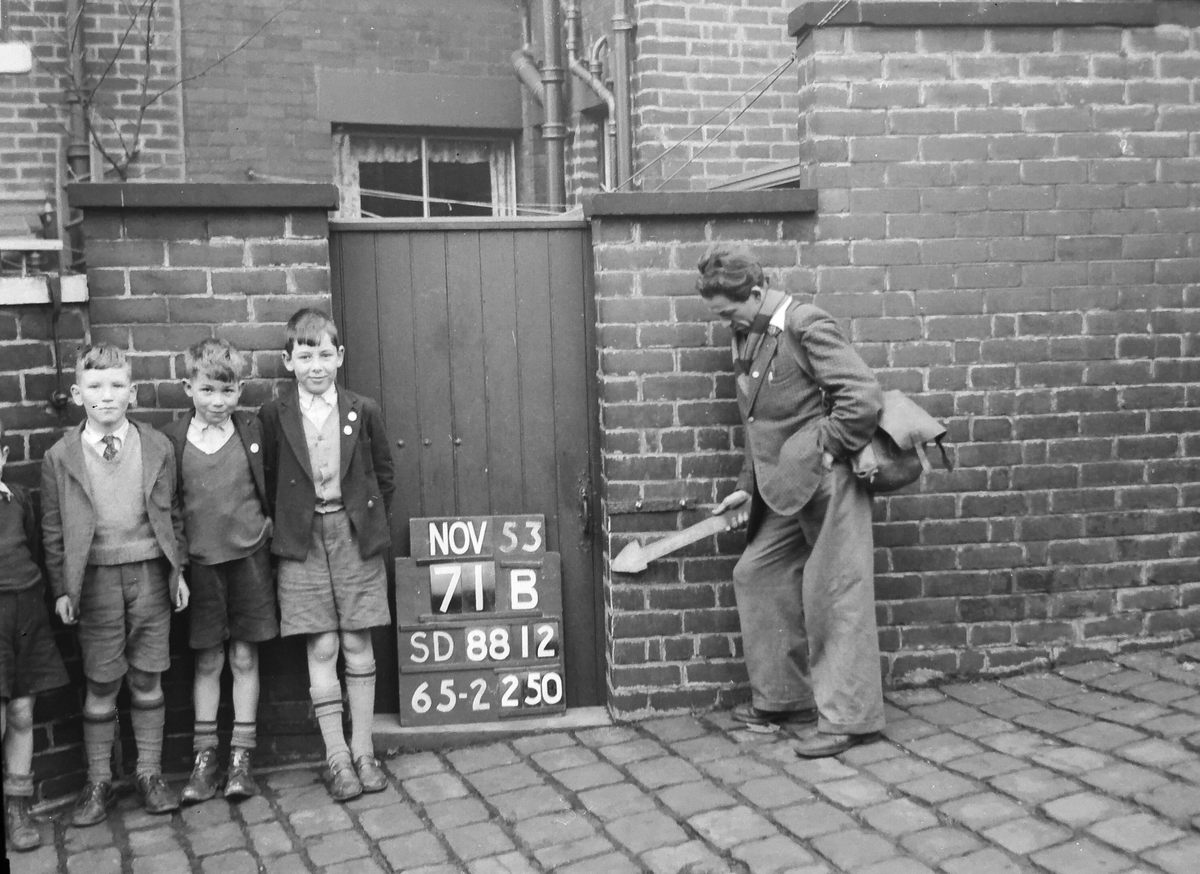 A trio of smiling boys photobomb this survey worker, who seems to be muffling a grin himself.