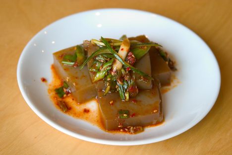 Acorn jelly is often seasoned with soy sauce and sesame oil, and comes topped with green onions, sesame seeds, and Korean chili flakes (gochugaru).