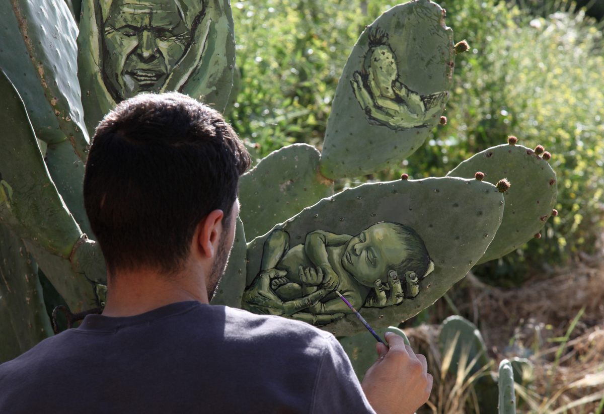 Palestinian artist Ahmed Yasin paints on a cactus at his house garden in the West Bank village of Aseera Ashmaliya near Nablus.