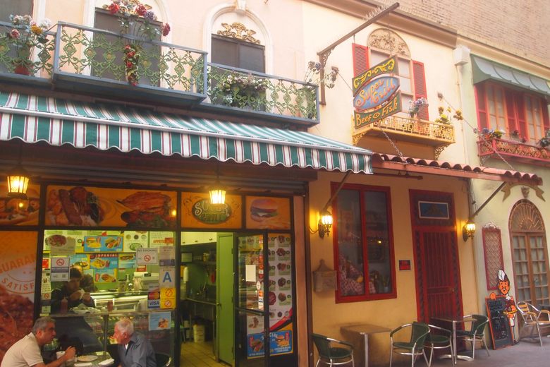 A European-style alley in Los Angeles with colorful storefronts, striped awnings, and outdoor cafe seating.