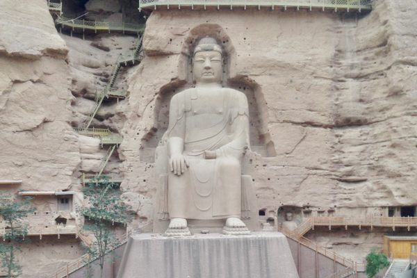 A massive seated Buddha is carved into a rock face.