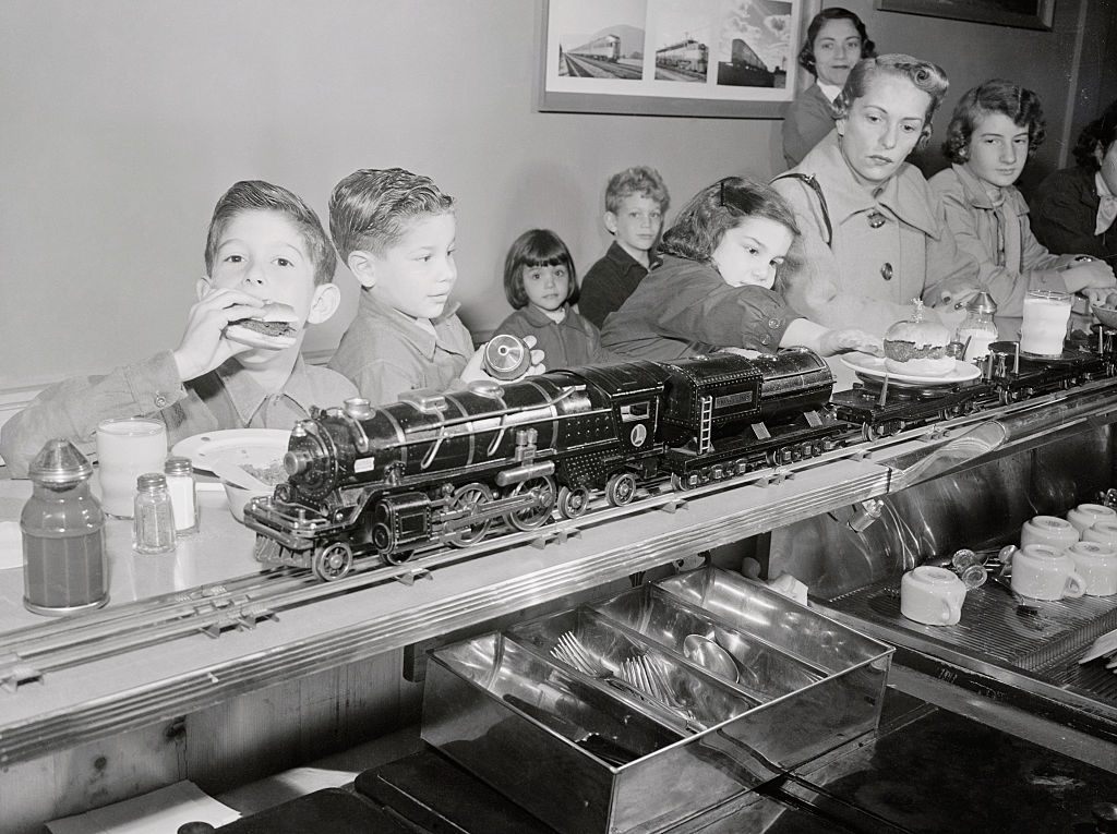 Children dive into train-delivered burgers at an early automated diner.