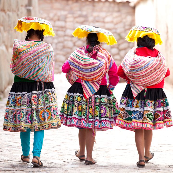Three women wearing traditional clothes passing the last remaining Inca wall in Cusco