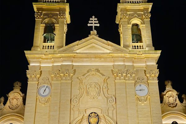 The façade of St. George’s Basilica at night shows the Alpha clock on the left and the Omega clock on the right.