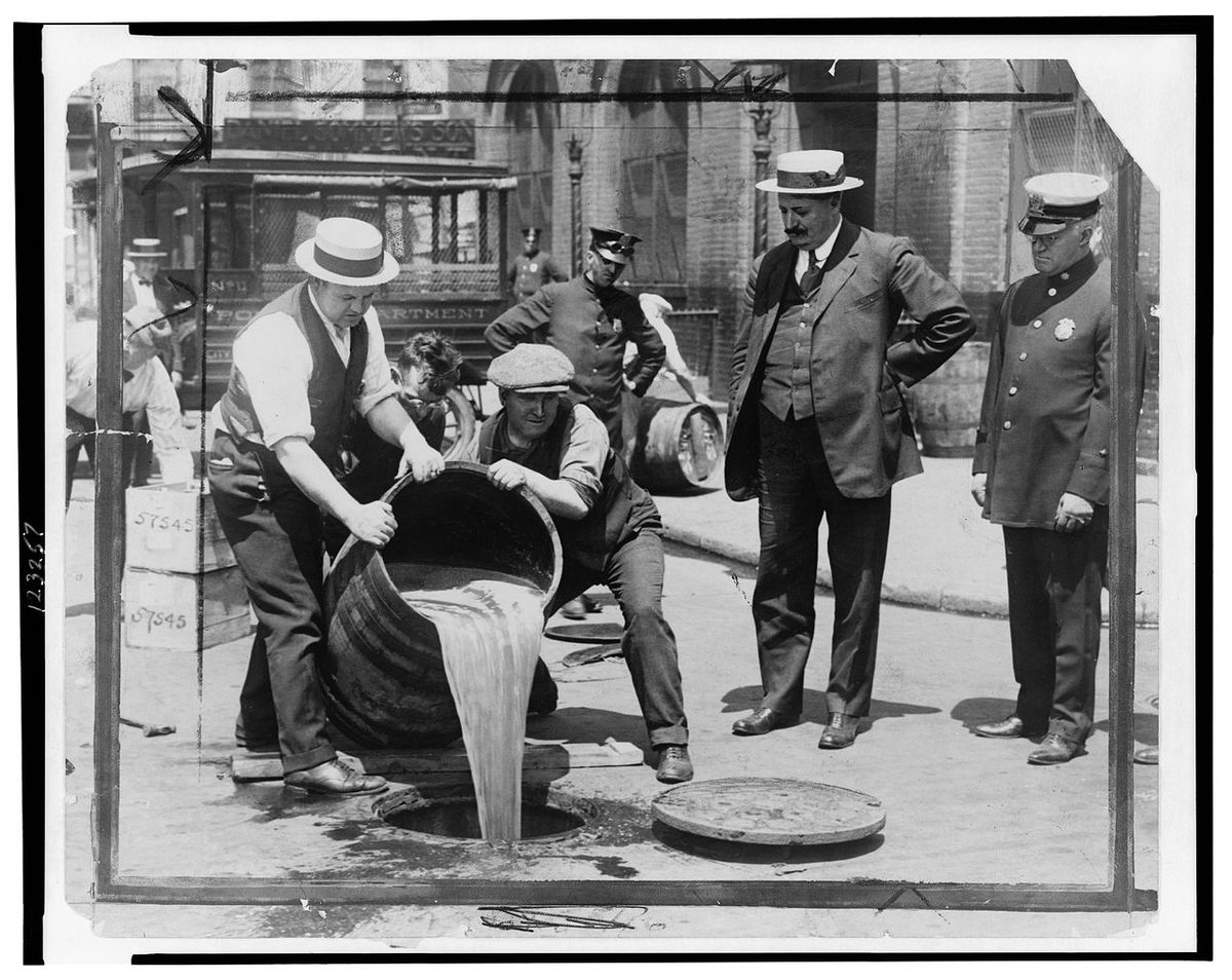 New York City Deputy Police Commissioner John A. Leach, right, watches over agents pouring liquor into the sewer after a raid.