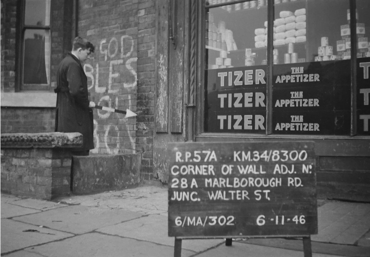 The graffiti behind this survey worker, "God Bless Our Boys," is likely from VE or VJ Day.